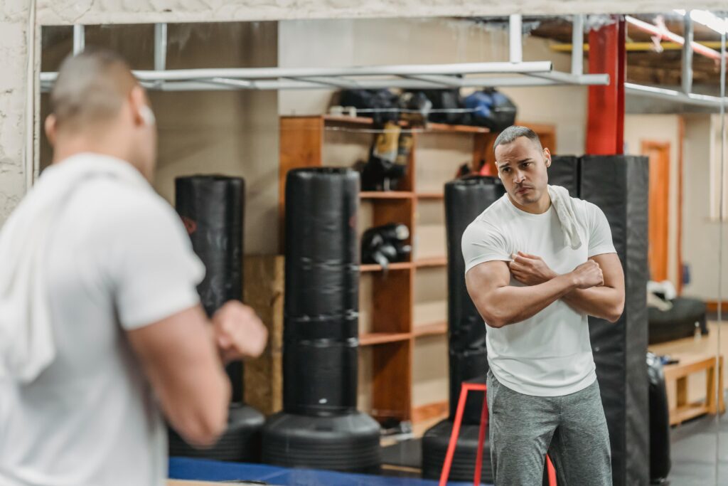 A muscular man stands in front of a gym mirror, reflecting on his progress during an intense workout session.